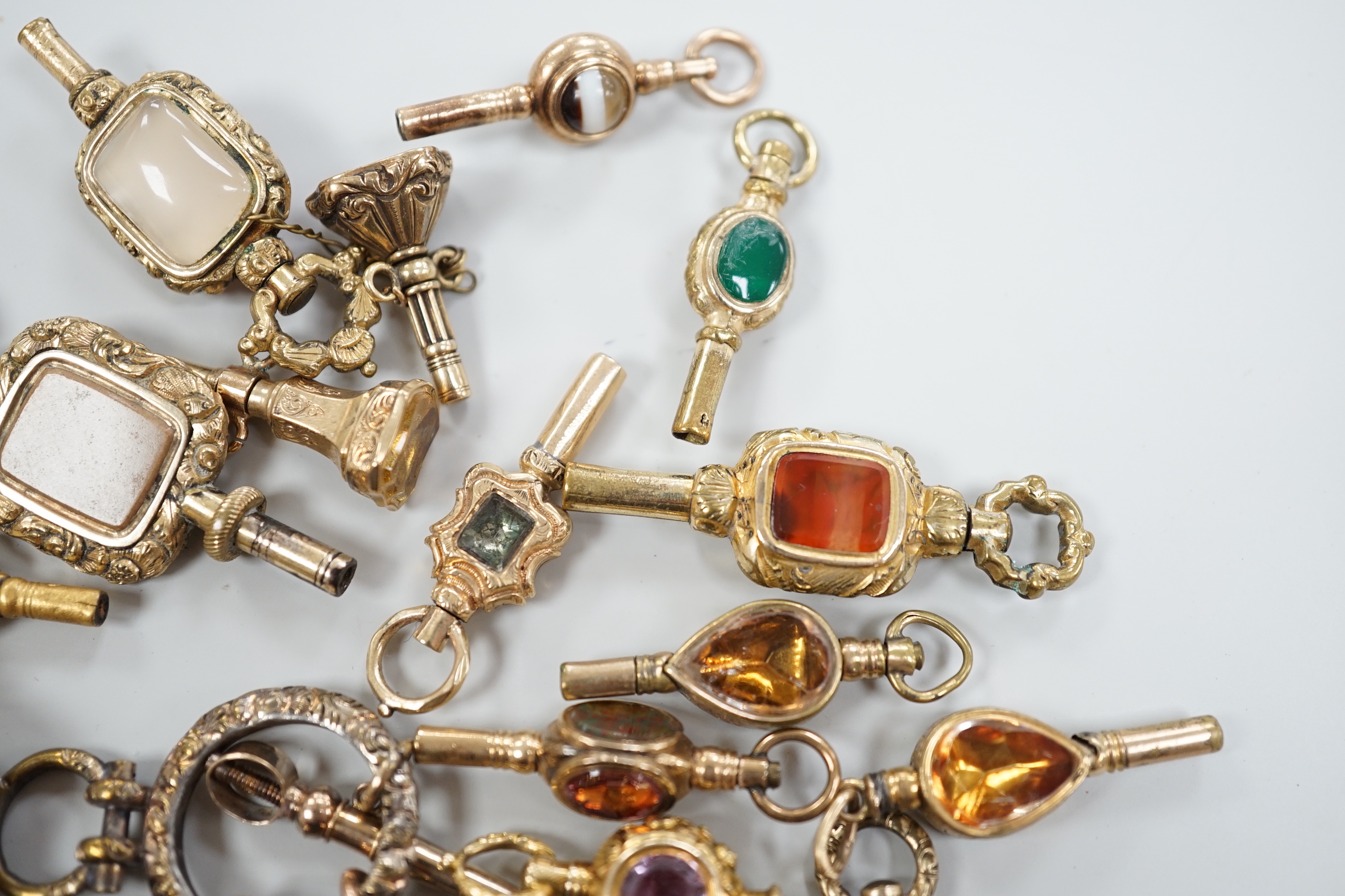 Sixteen assorted 19th century yellow metal overlaid and mainly gem set small watch keys, including chalcedony, citrine, amethyst, banded agate, bloodstone and a ring with four keys attached, largest 47mm.